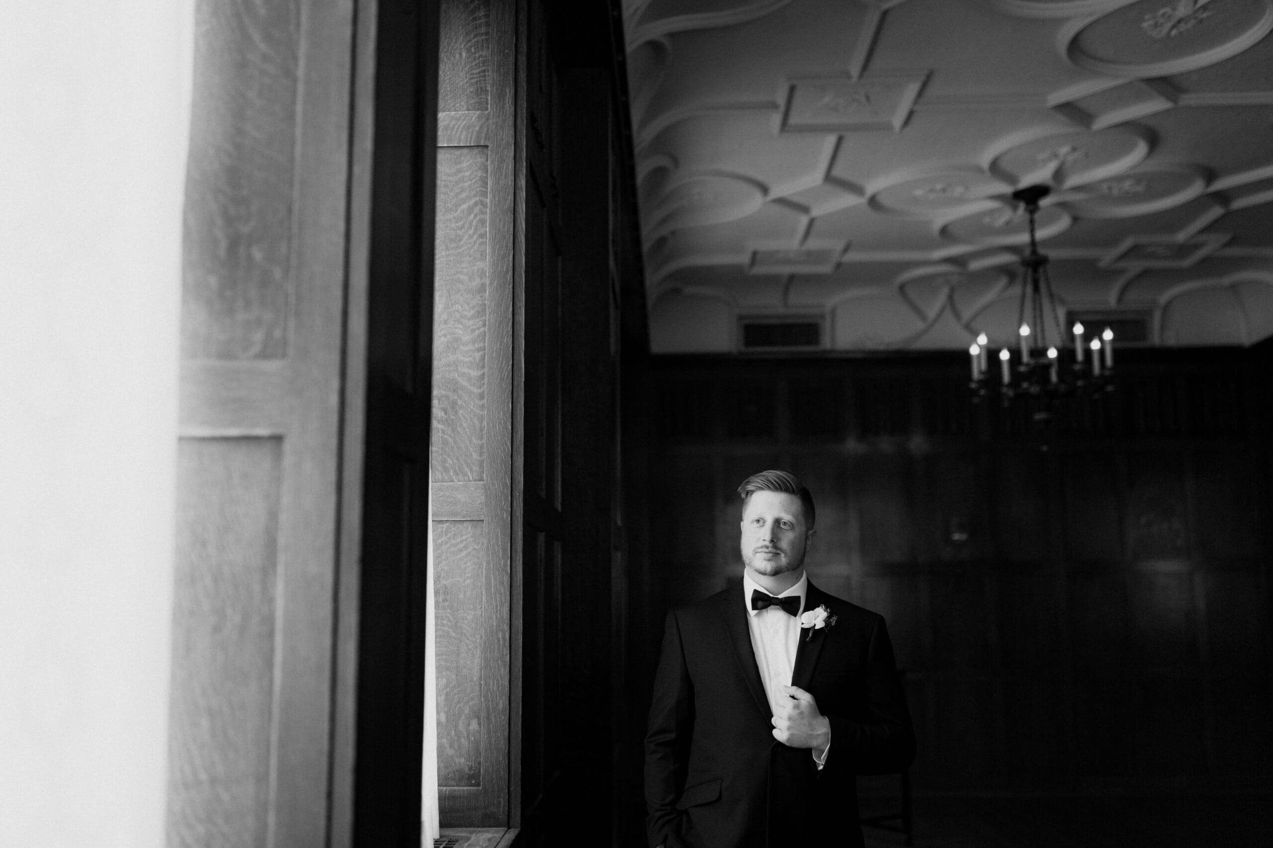 Groom standing in front of a window holding his jacket