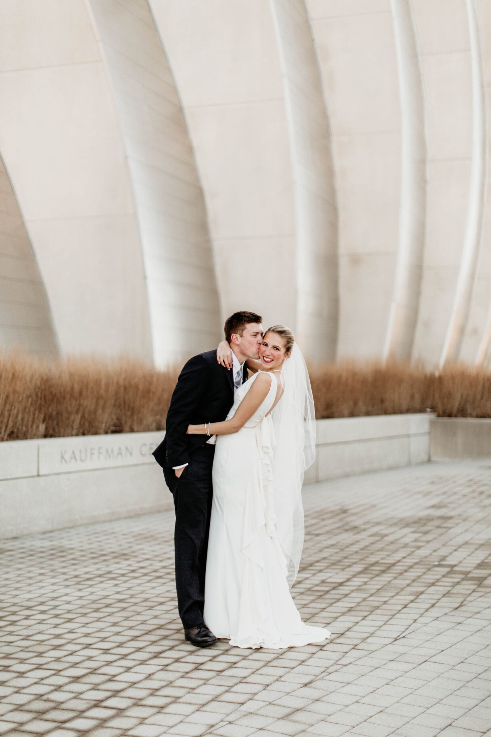 Groom kissing bride on cheek during bridal party portraits.