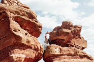 Engaged couple sitting on red rocks at Garden of the Gods, looking out over the scenic Colorado landscape.