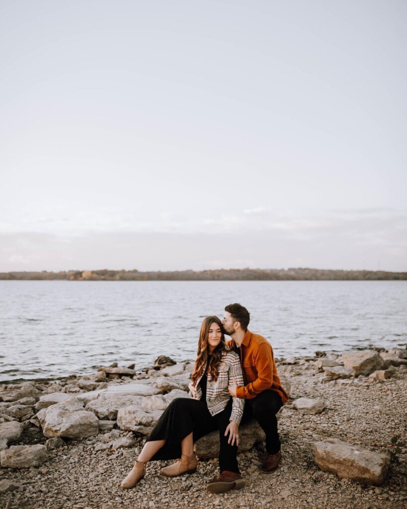 Couple sitting in front of Kansas City, MO lake for engagement p hotos 