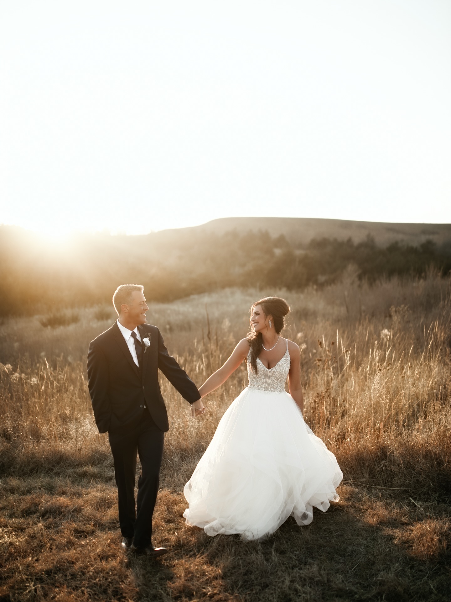 birde and groom walking in field in front of mountains